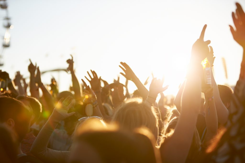 Vários jovens com mãos pra cima vistos de costas curtindo festival de música